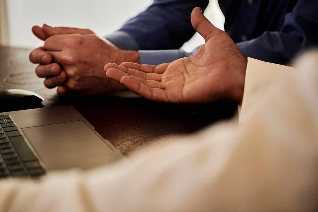 Ein Businessmann reicht einem anderen Mann am Tisch sitzend seine Hand für einen Deal.