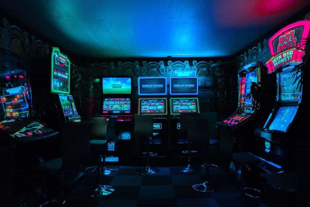 In einer verdunkelten Spielothek stehen nebeneinander sieben Automatenspielgeräte mit bunt blinkenden Lichtern.