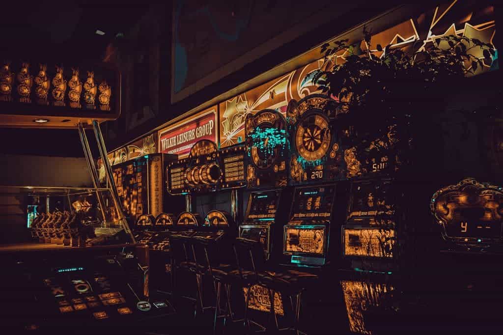 In einem verdunkelten Casino stehen golden leuchtende Automaten aneinandergereiht.