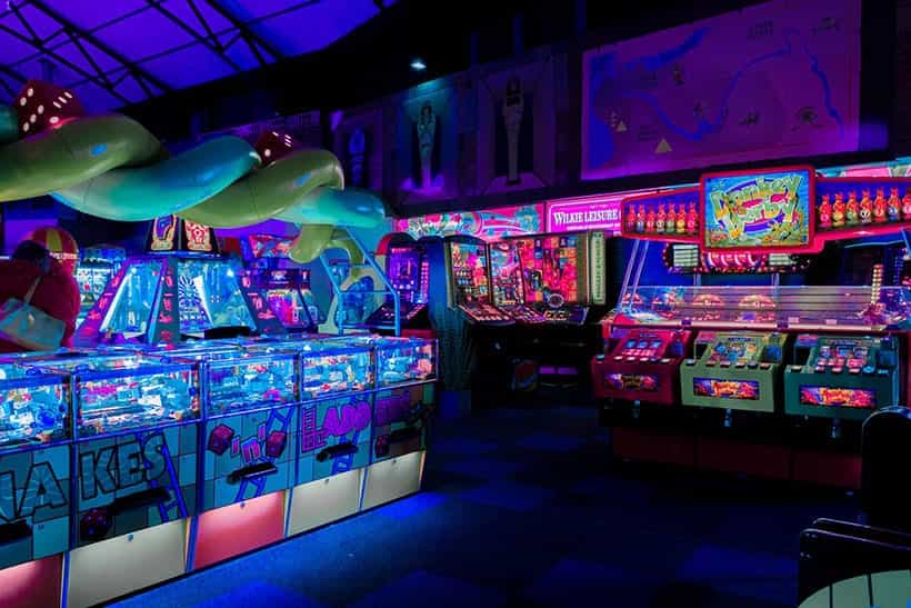 In einer Spielothek sind zahlreiche bunt leuchtende Spielautomaten im Dunkeln aufgestellt.