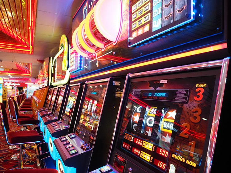 Nebeneinanderstehende hauptsächlich rötlich leuchtende Spielautomaten in einem Casino.